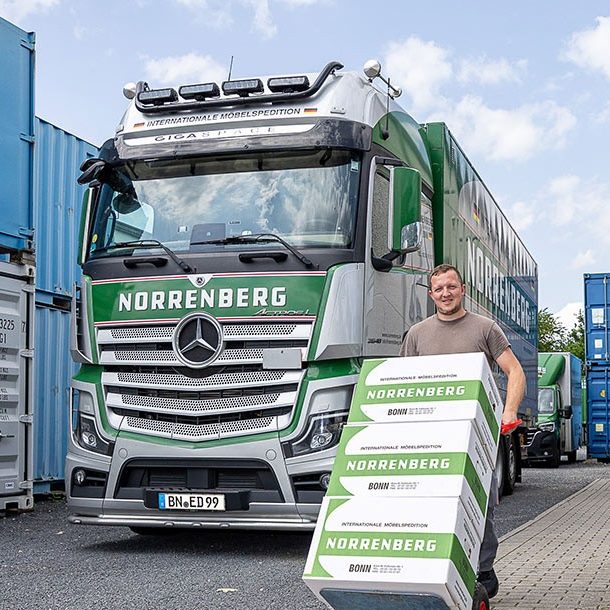 Mann mit Kartons vor LKW und Containern.