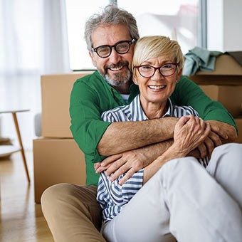 Senioren umarmen sich, im Hintergrund stehen viele Kartons